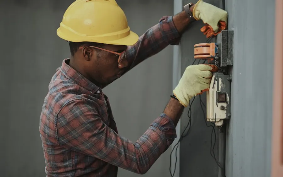 Tradesperson in a hard hat wiring an electrical panel on a job site